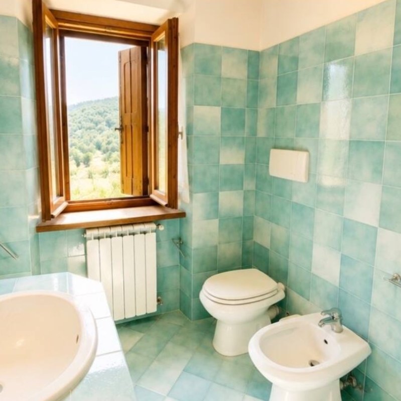 Bagno con piastrelle azzurre, vasca e finestra aperta sul bosco