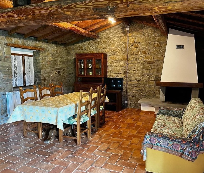 Sala con muri in pietra, travi in legno, tavolo da pranzo, divano e camino